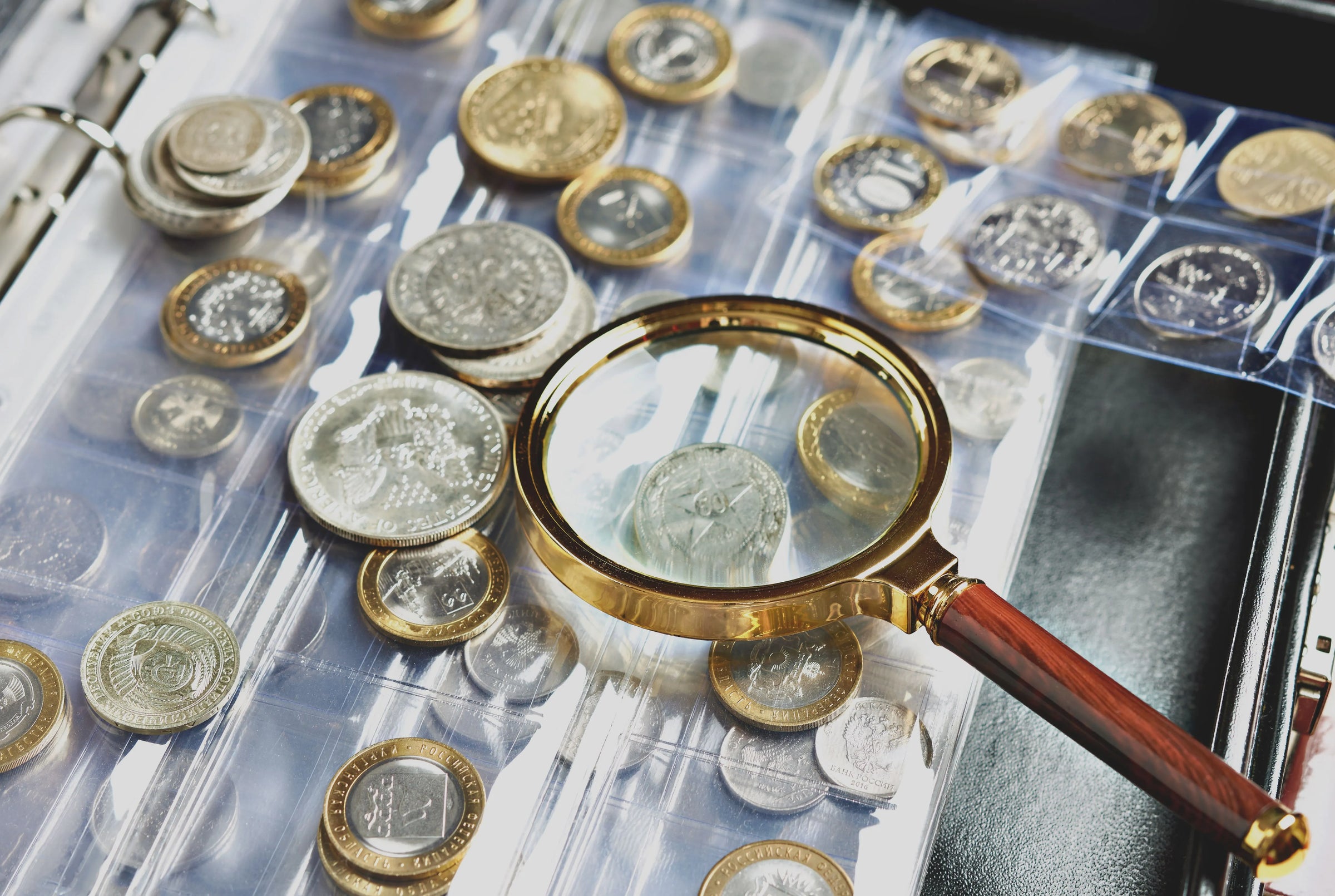 An image of a magnifying glass on top of a lot of mixed foreign coins.